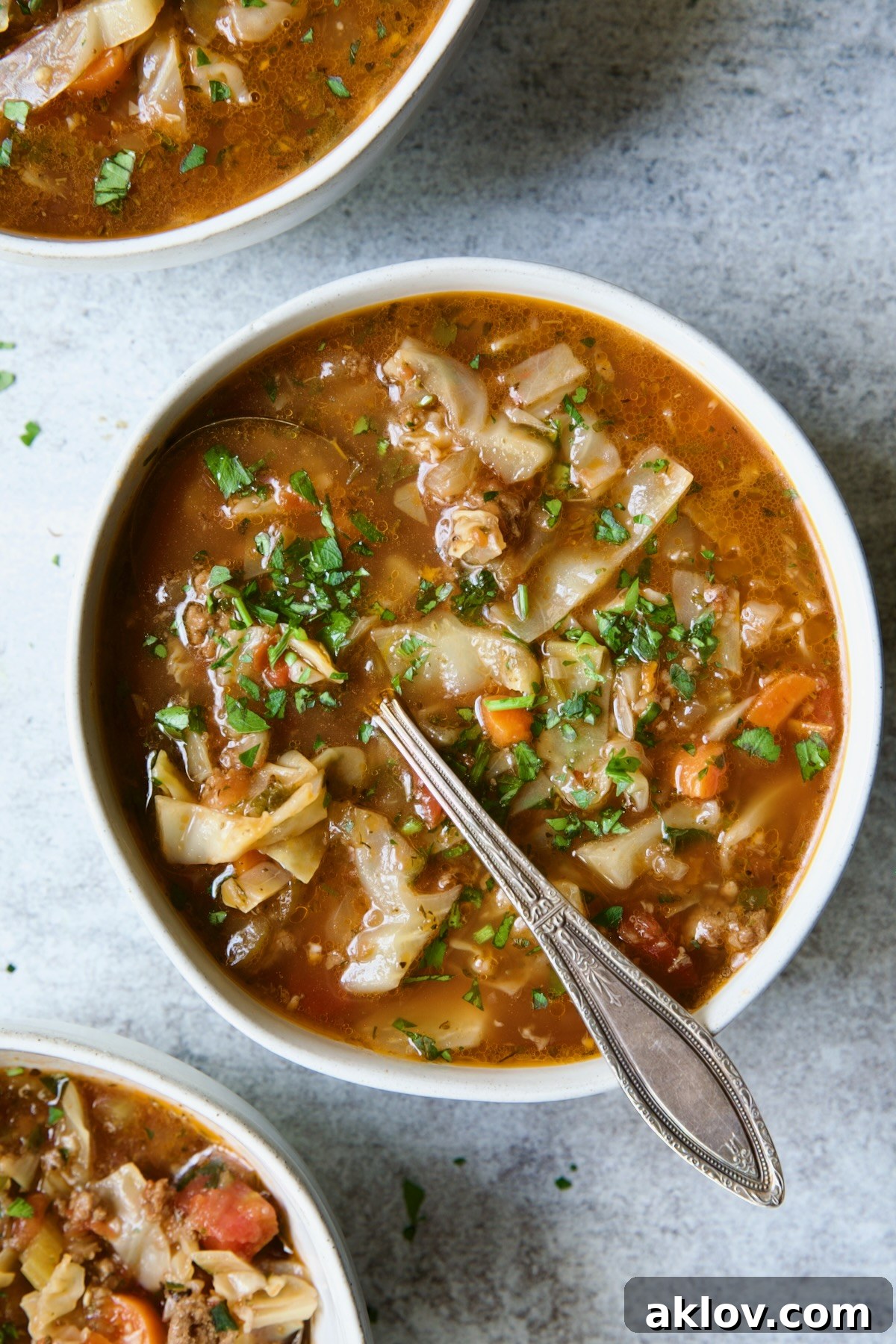 One serving of Beef and Cabbage Soup in white soup bowl with soup spoon.