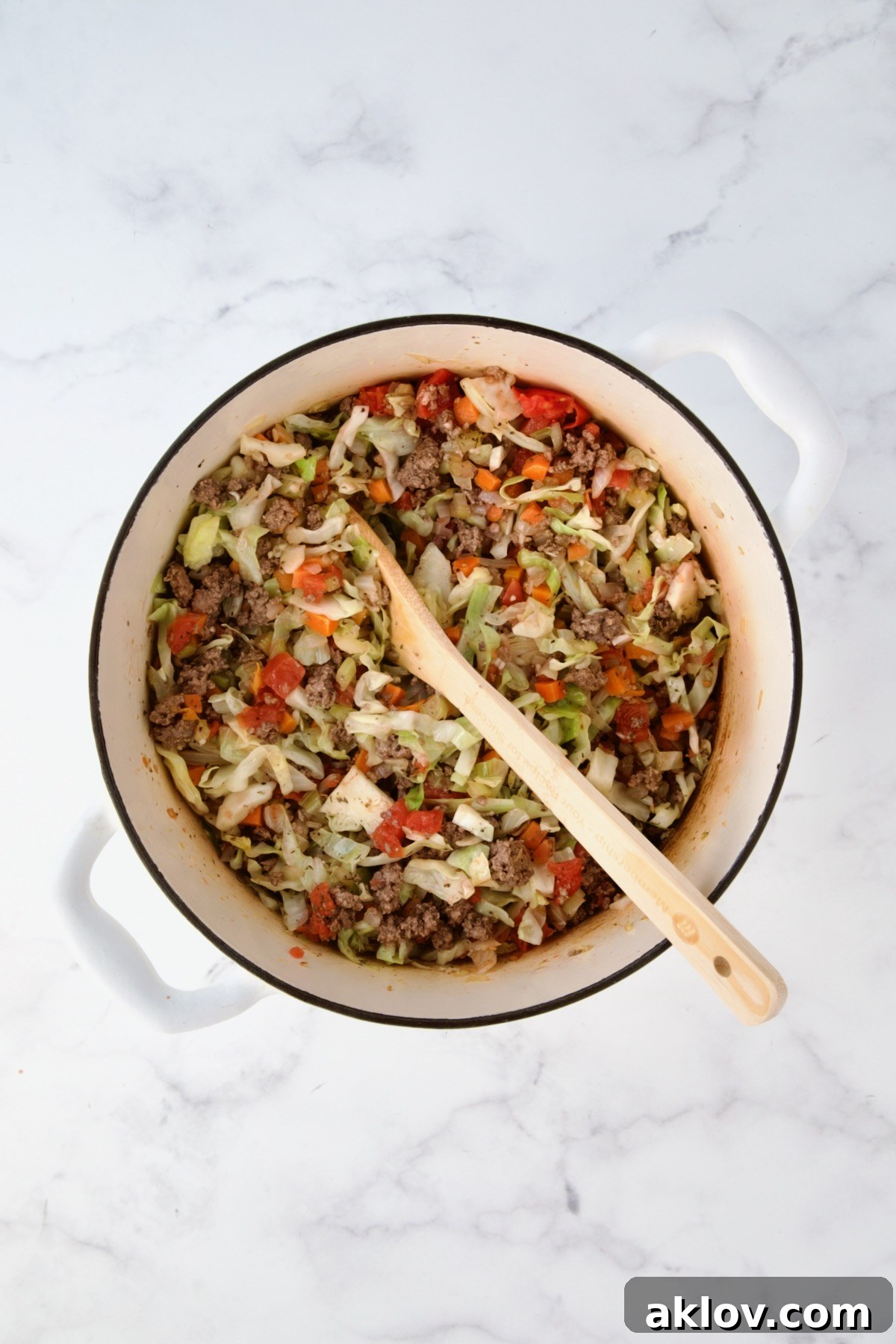 Cooked ground beef added to onions, carrots, celery and cabbage in white Dutch oven.