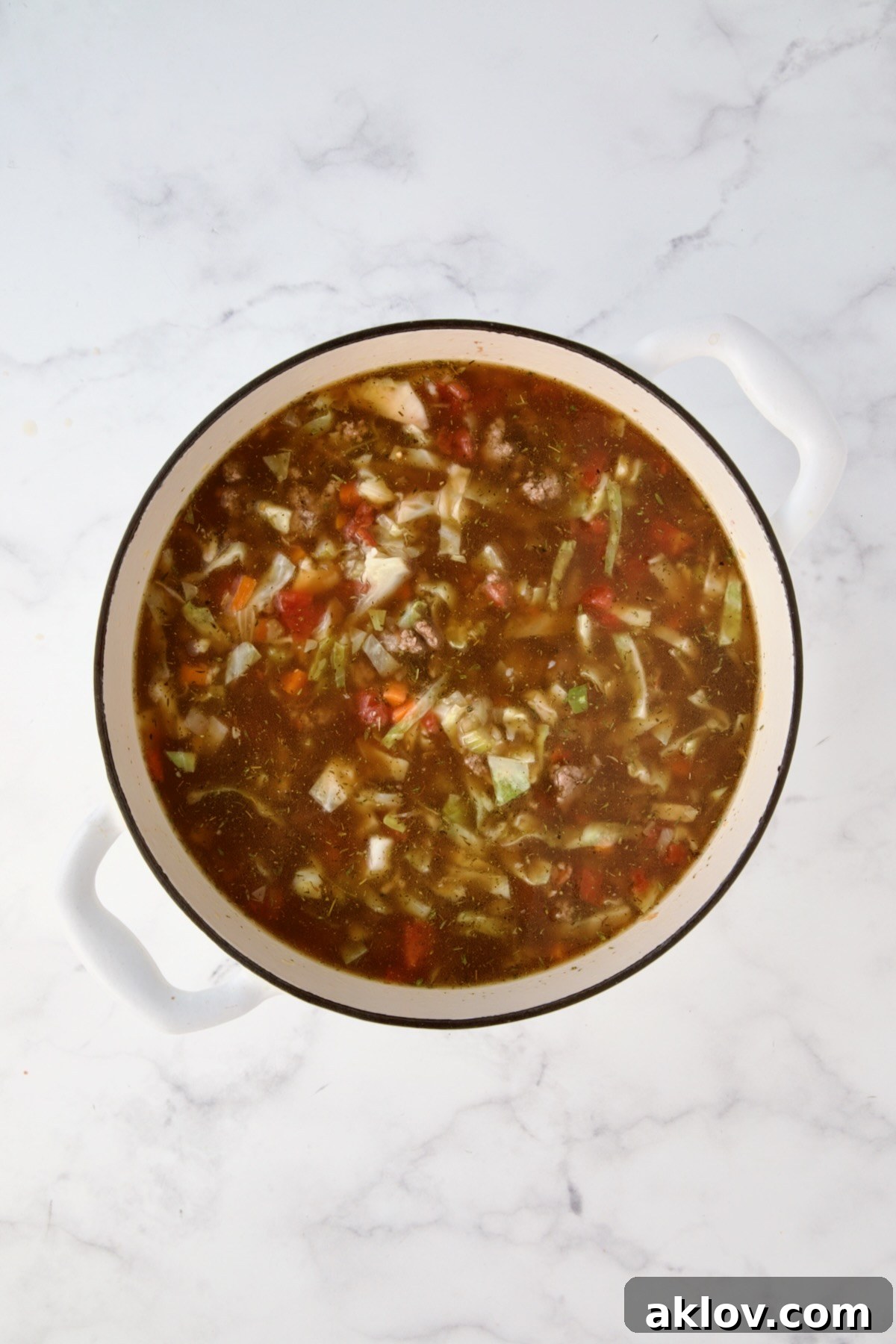 Beef broth, diced tomatoes, tomato sauce and herbs added to vegetables and beef in white Dutch oven.