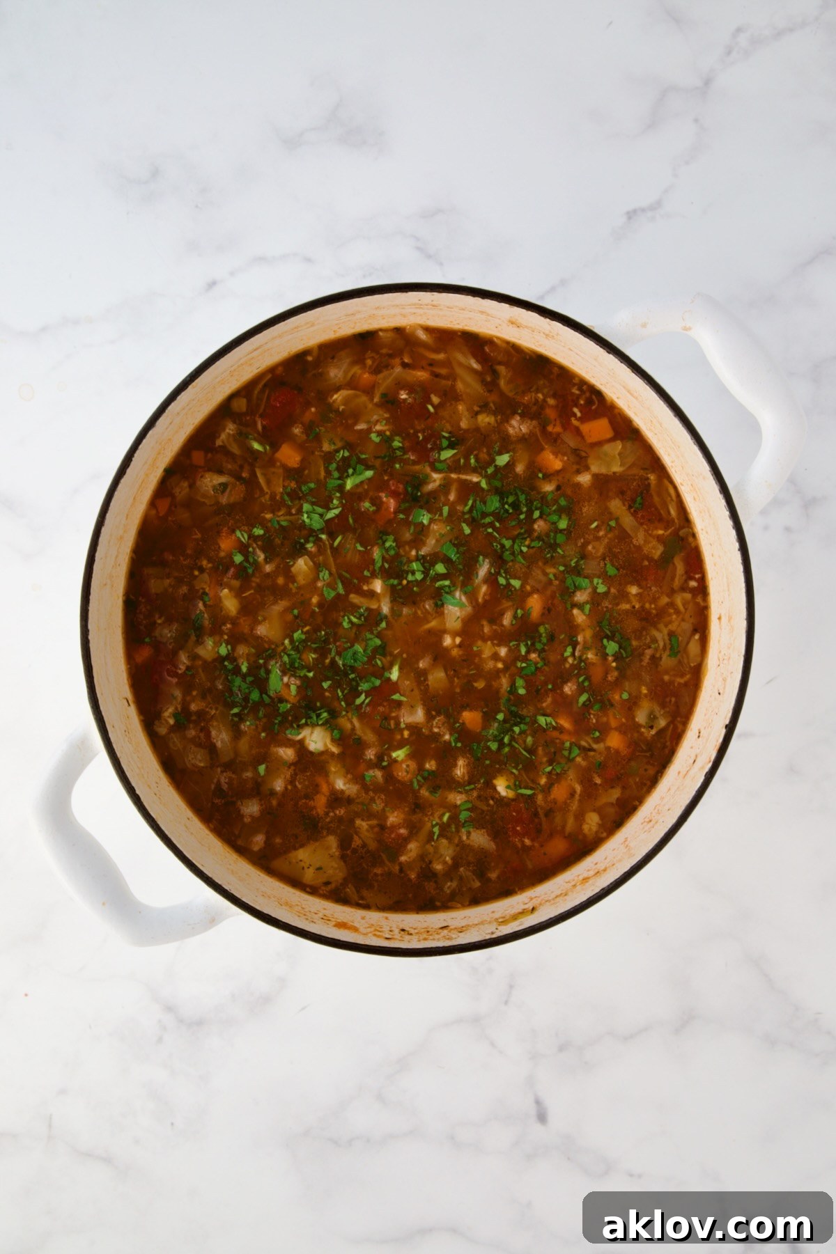 Finished Beef and Cabbage Soup garnished with parsley in white Dutch oven.