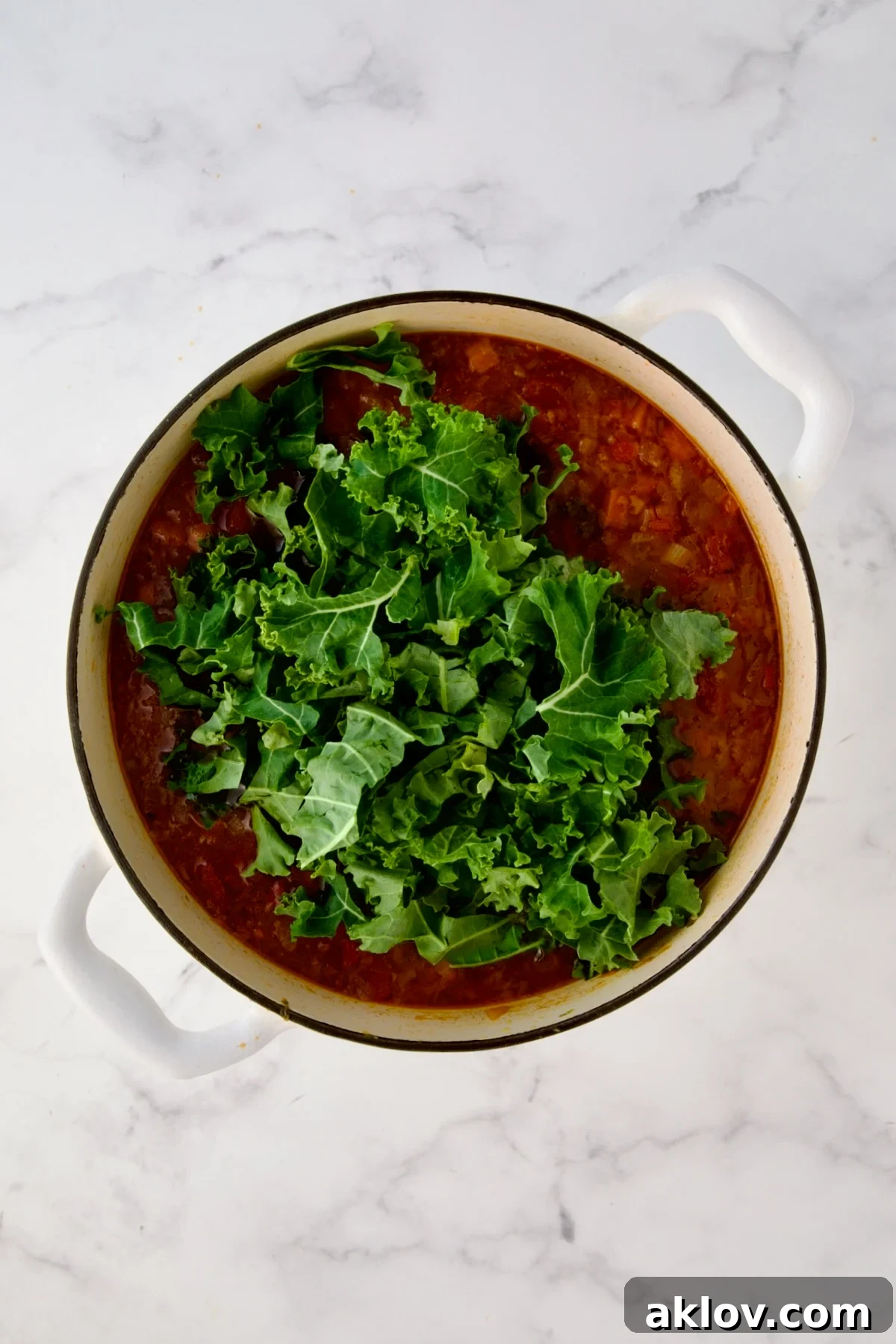 Kale added to soup in white enamel Dutch oven.