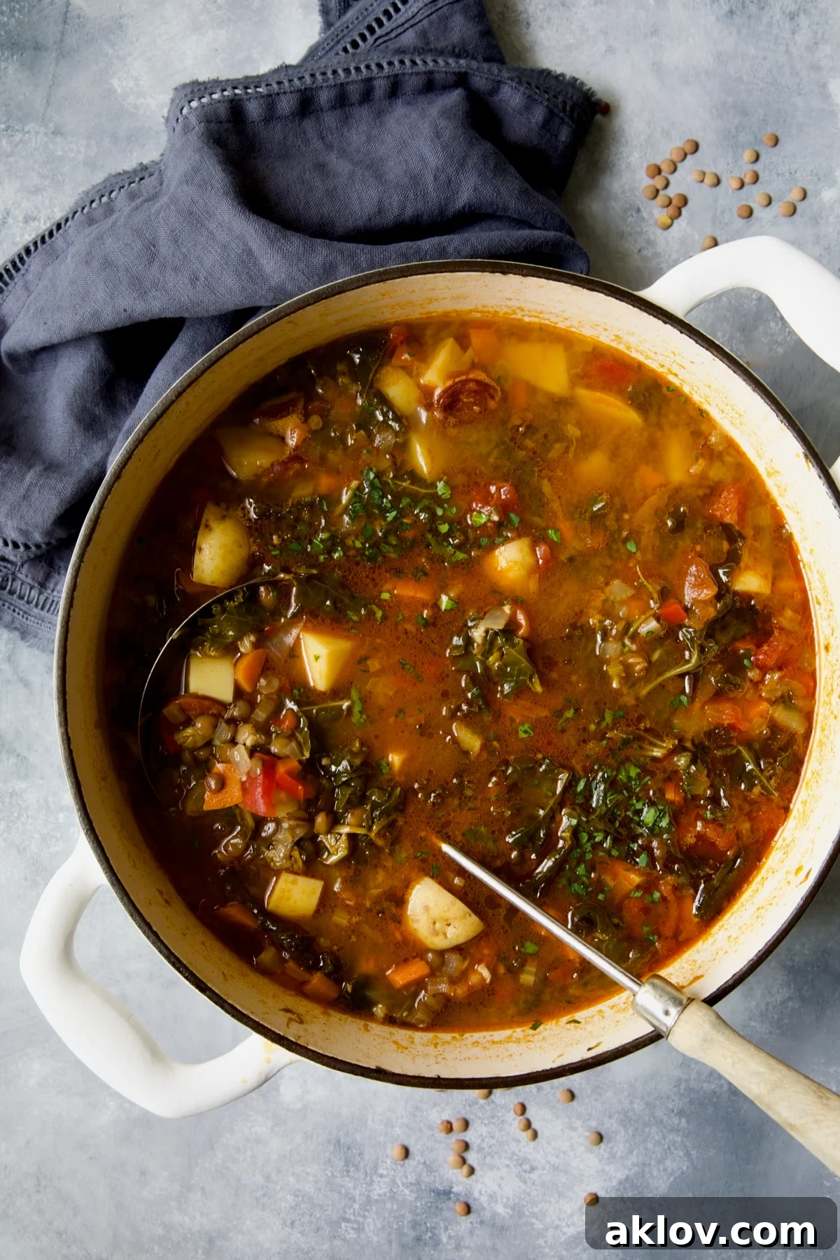 Finished Spanish Lentil Potato Soup in a white enamel Dutch oven with a soup ladle.