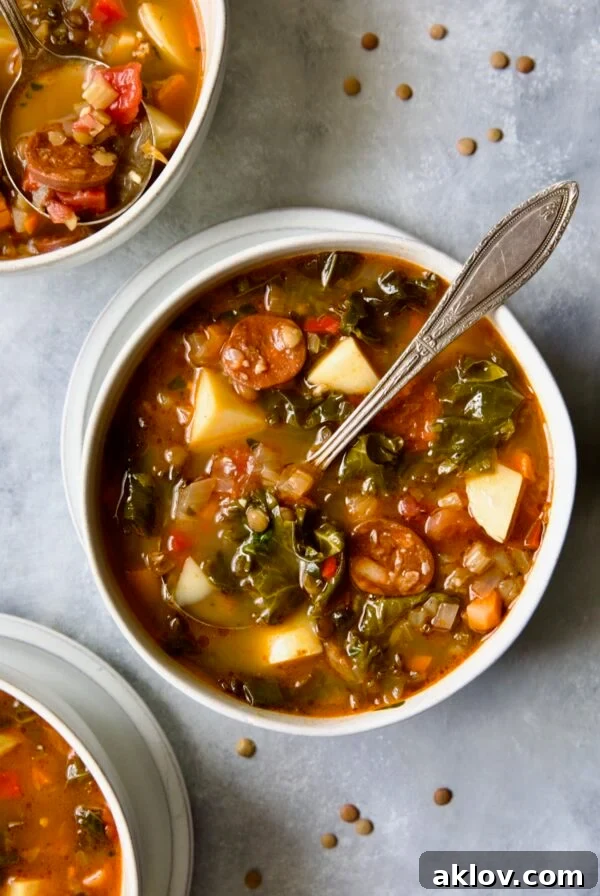 One serving of Spanish Lentil Potato Soup in white bowl with soup spoon with lentils scattered about.
