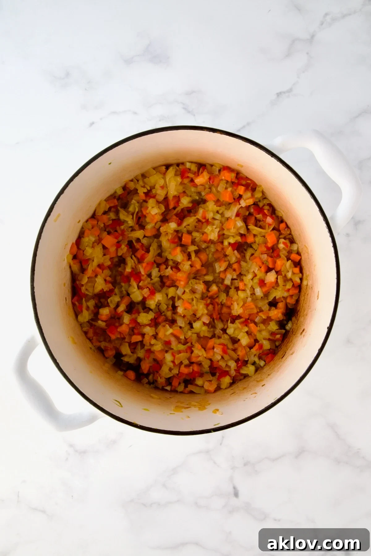 Cooked onions, celery, red bell pepper and carrots in white enamel Dutch oven.