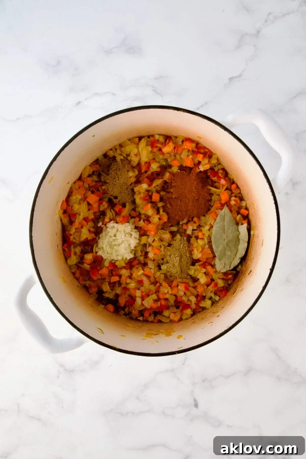 Cooked onions, celery, red bell pepper and carrots in white enamel Dutch oven with herbs and spices added.