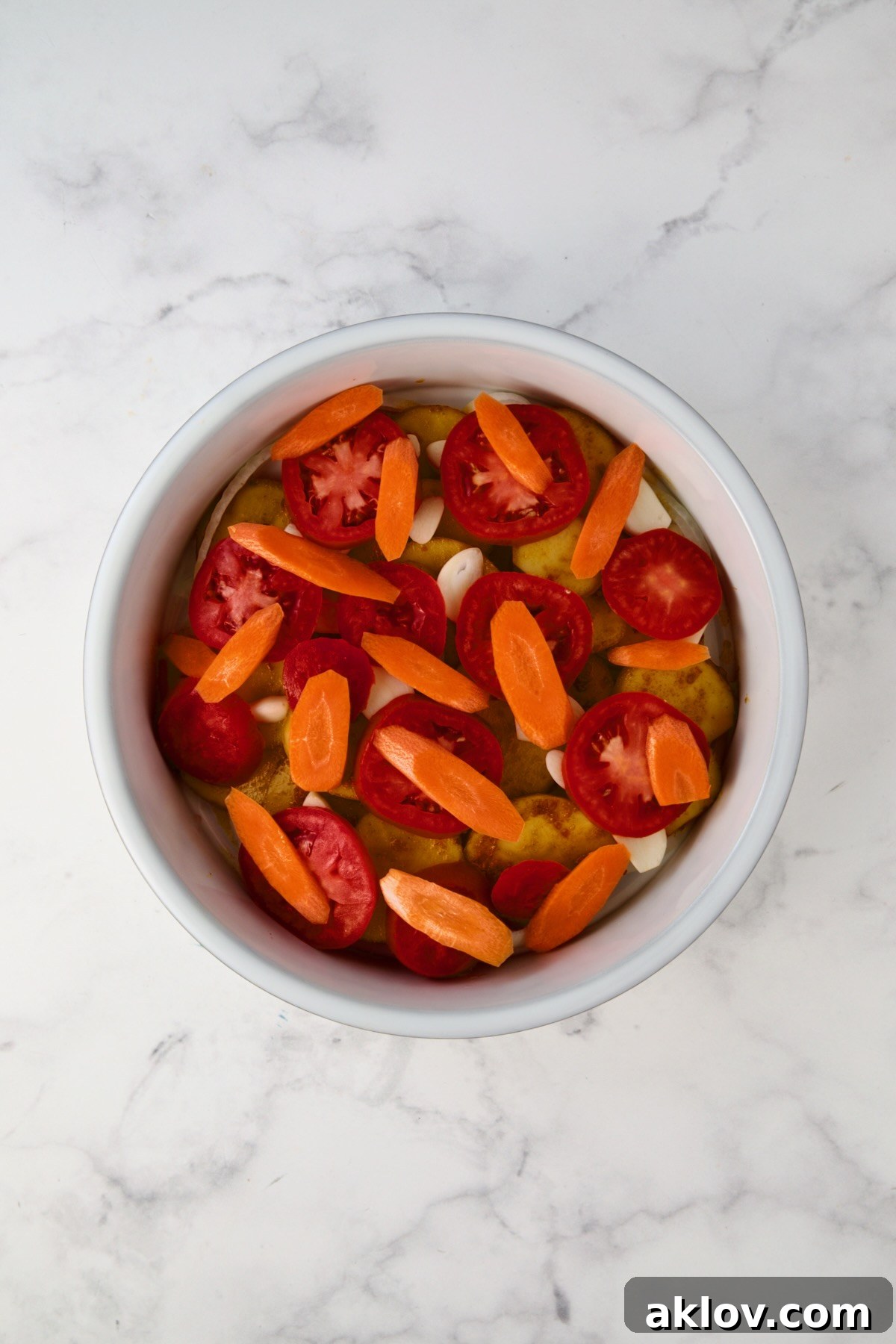 Carrots placed over tomatoes in round white baking dish.