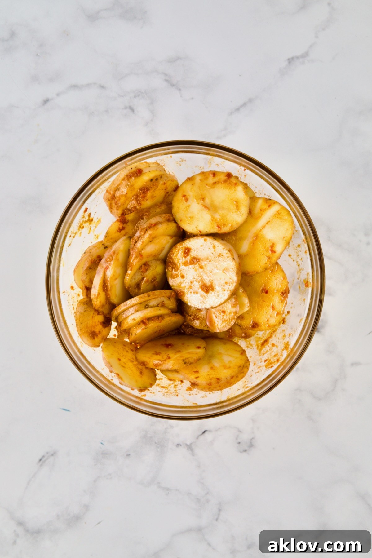 Potatoes tossed with spice and oil combination in glass bowl.