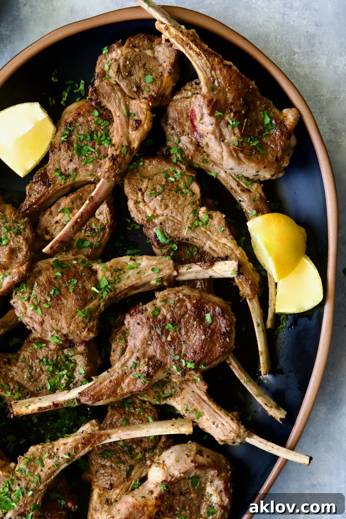 Greek Lamb Chops on black oval platter garnished with lemon wedges.