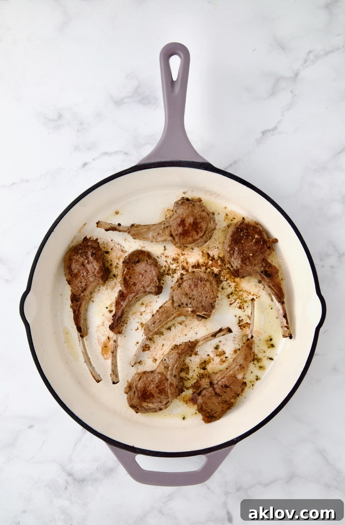 Seven seared lamb chops in white enamel cast iron skillet.