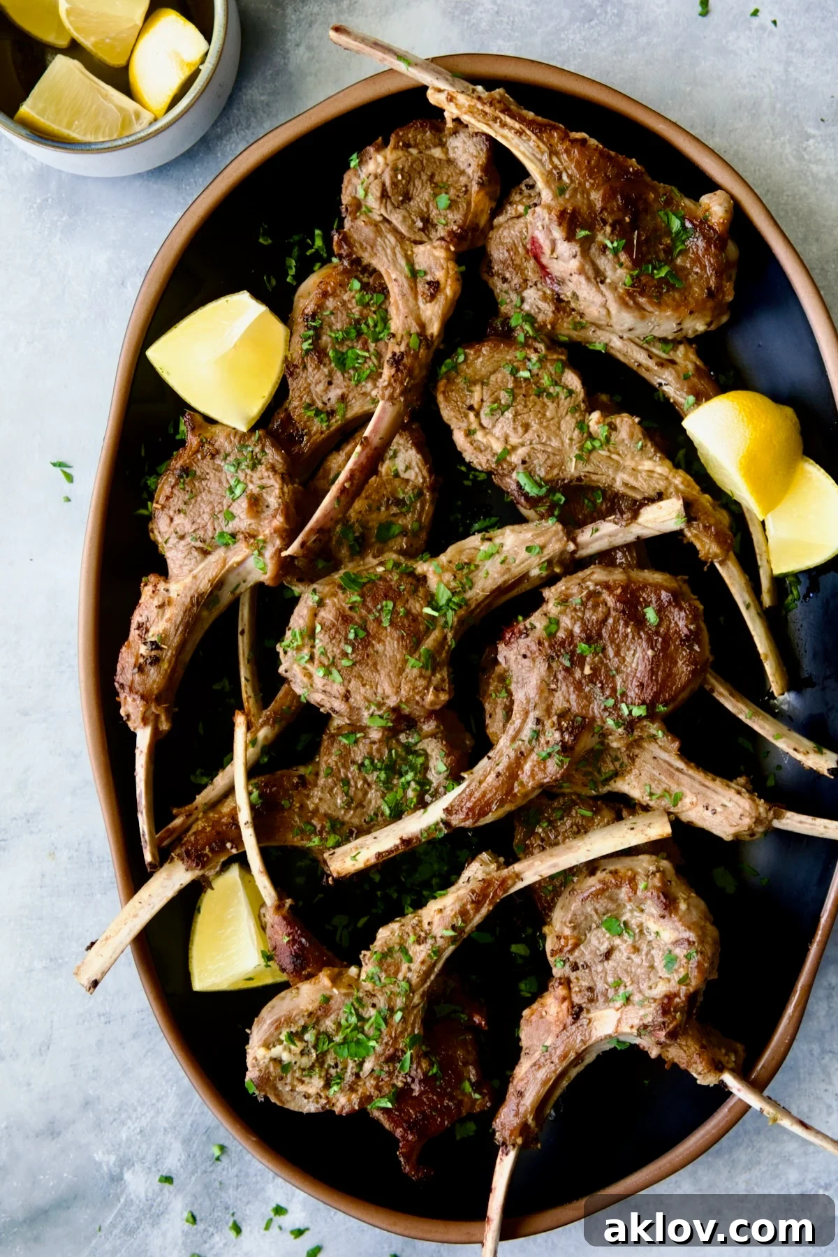 Greek Lamb Chops on black oval platter garnished with lemon wedges.