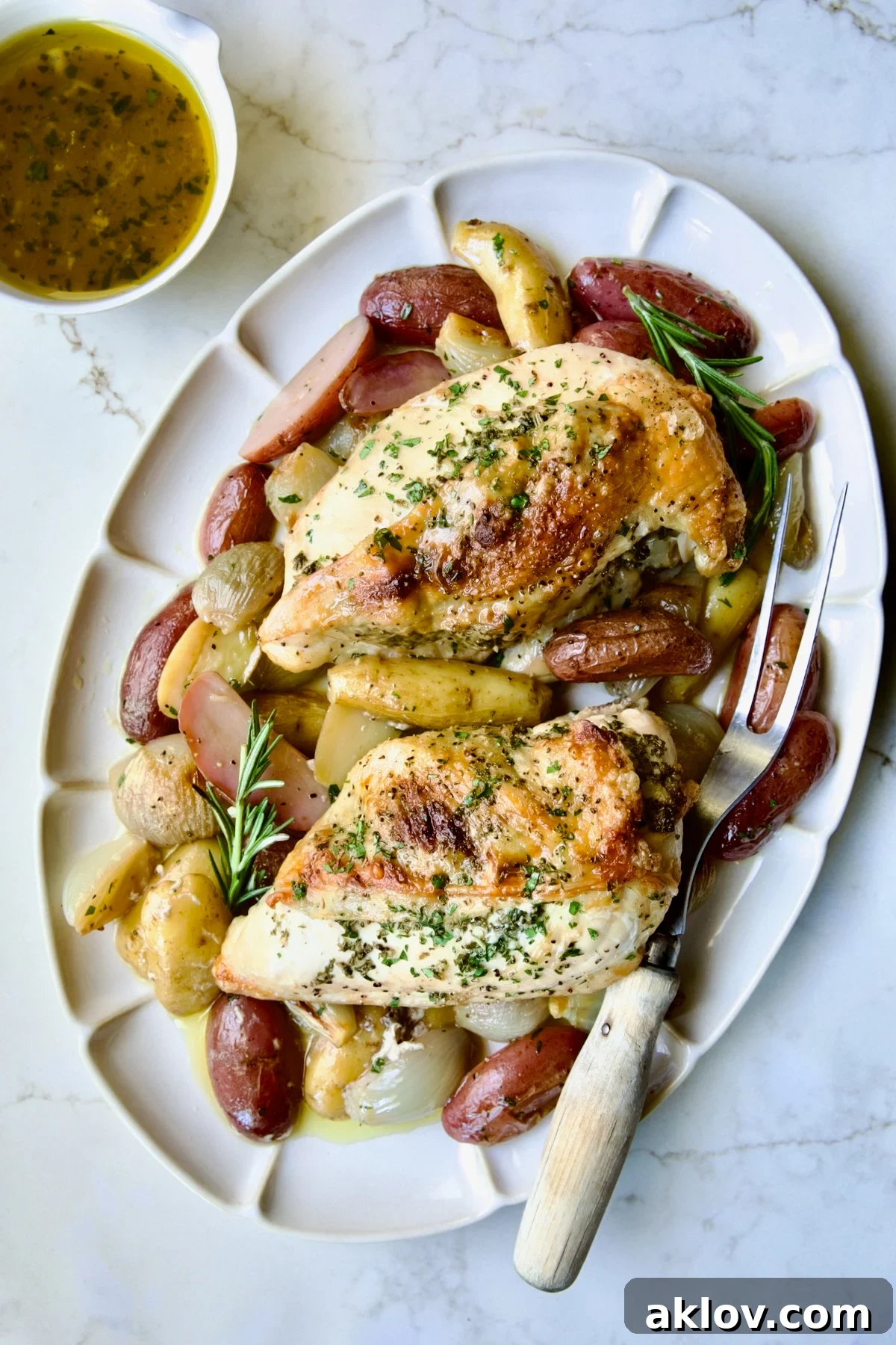 Two Roast Split Chicken Breasts with Potatoes and Shallots on white oval platter with meat fork.