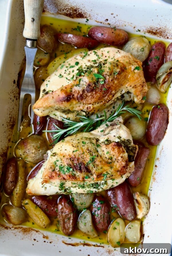 Two Roast Split Chicken Breasts with Potatoes and Shallots in white rectangular baking dish.