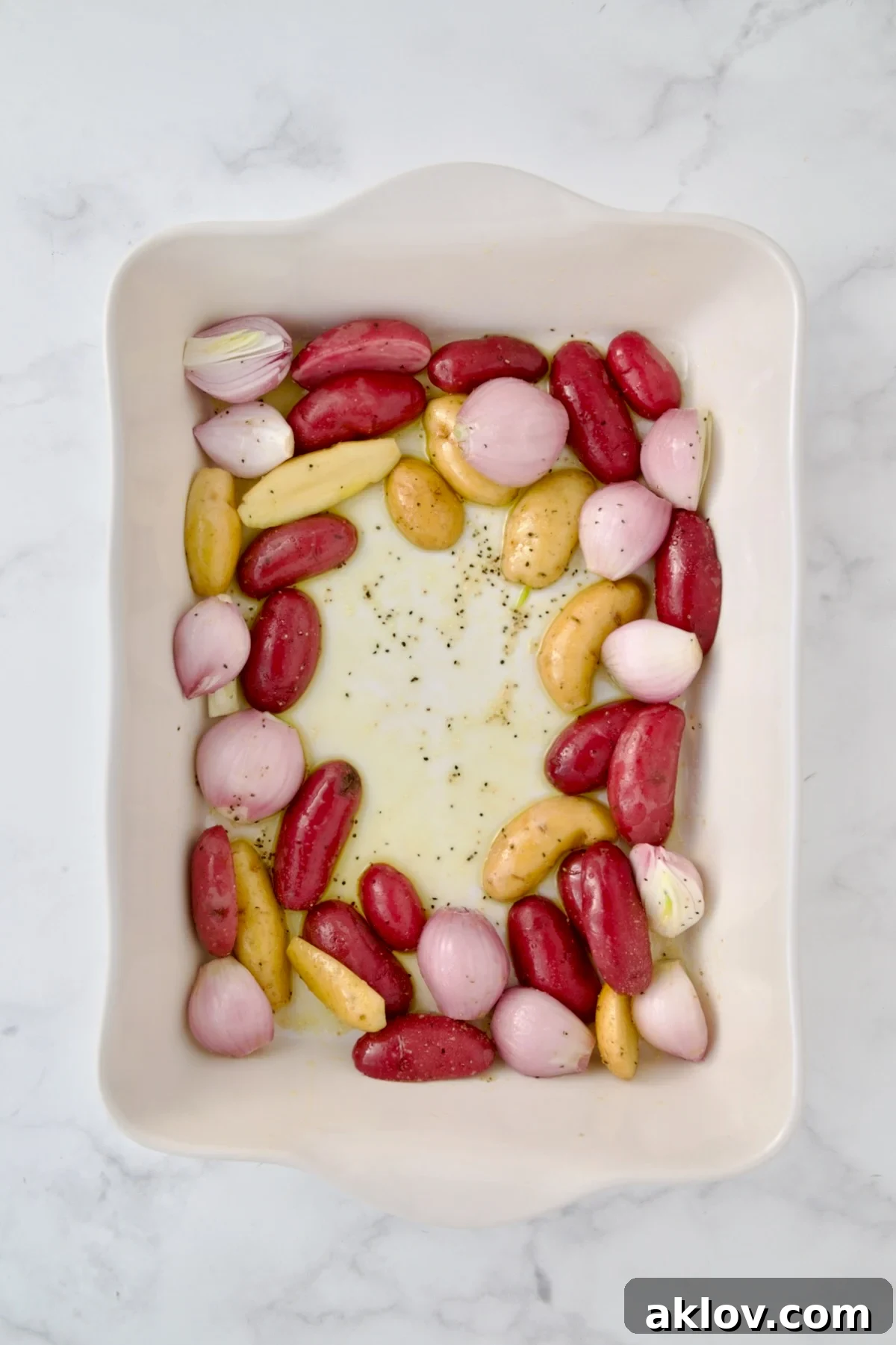 Uncooked potatoes and shallots in white rectangular baking dish.