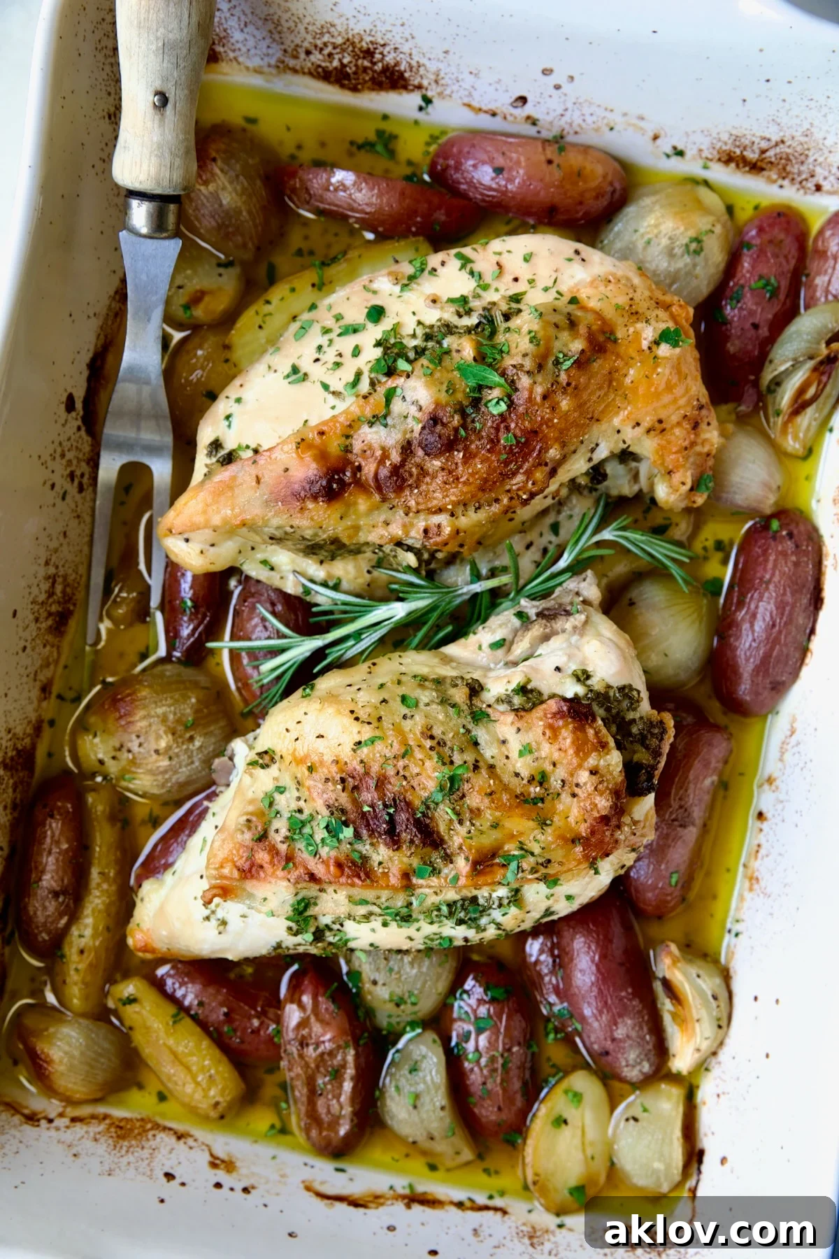 Two Roast Split Chicken Breasts with Potatoes and Shallots in white rectangular baking dish.