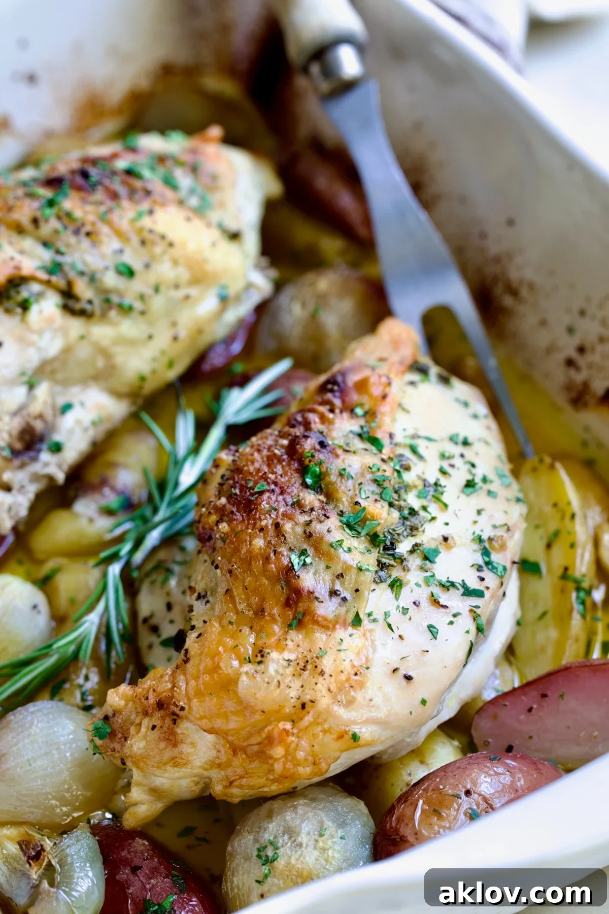 Close-up of Roast Split Chicken Breasts with Potatoes and Shallots on platter with meat fork.