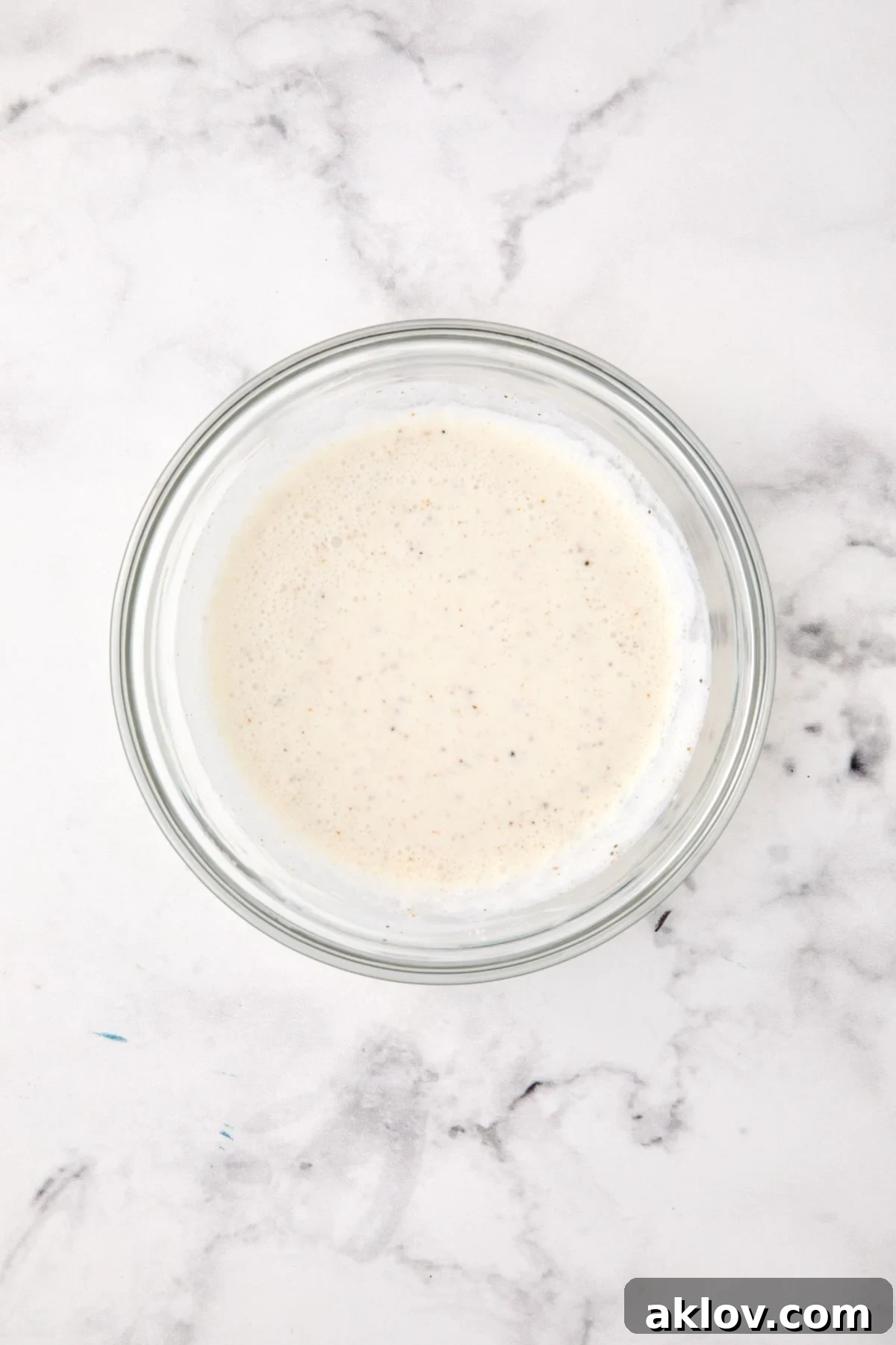 Creamy white wine sauce mixture in a clear glass bowl, ready to be poured.