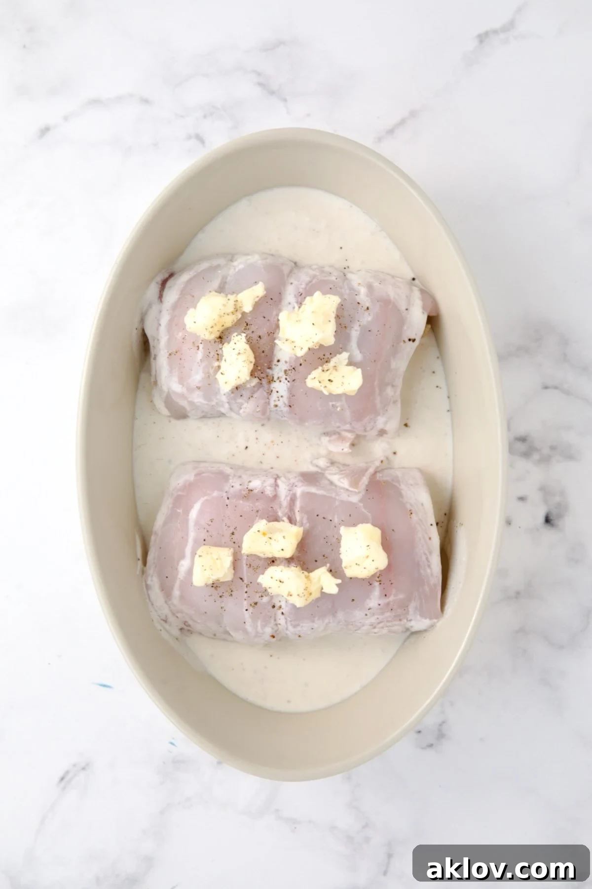 Two uncooked Crab-Stuffed Flounder pieces in an oval baking dish, generously dotted with butter, ready for the oven.