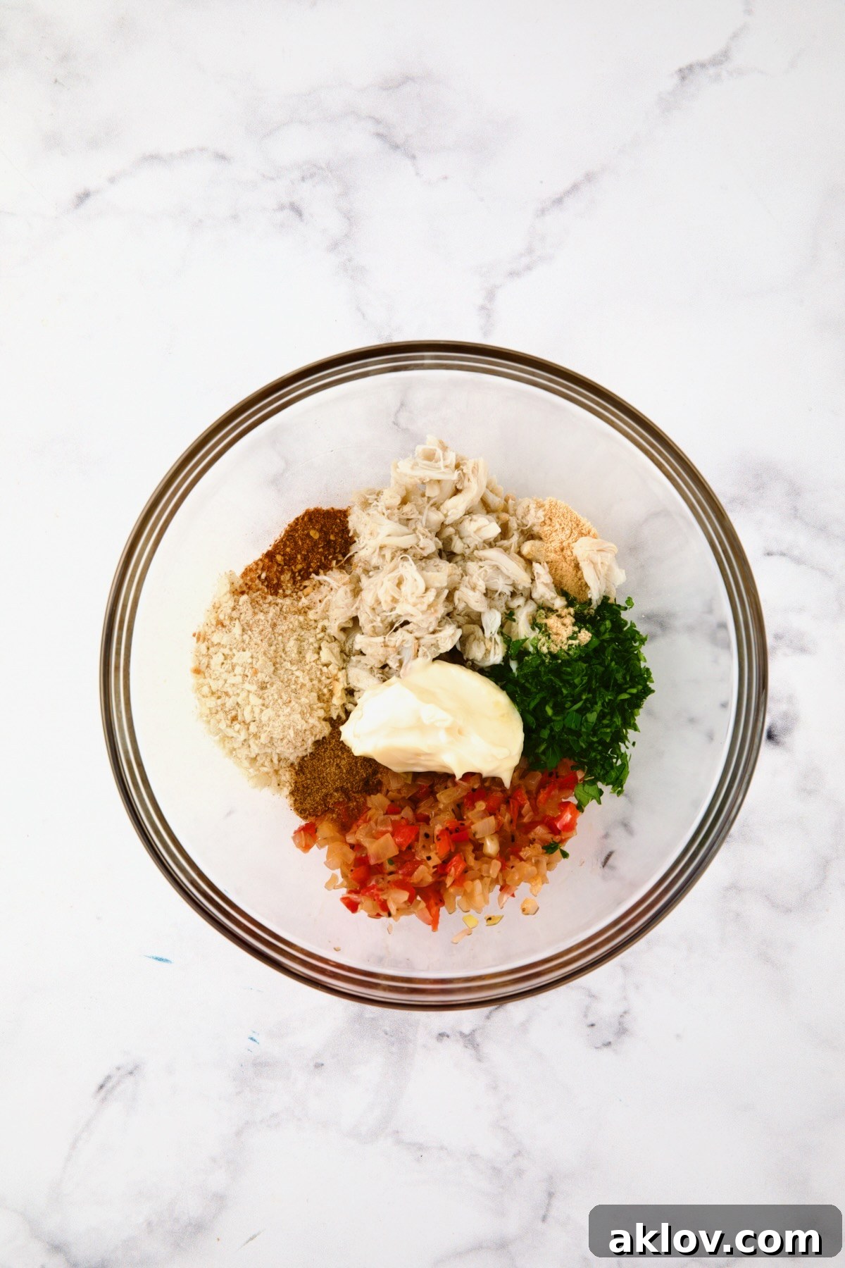 Individual ingredients for crab filling awaiting combination in a glass bowl.