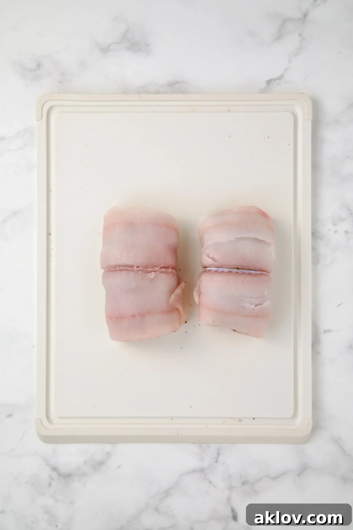 Two flounder fillets, expertly rolled to enclose the crab filling, resting on a white cutting board.
