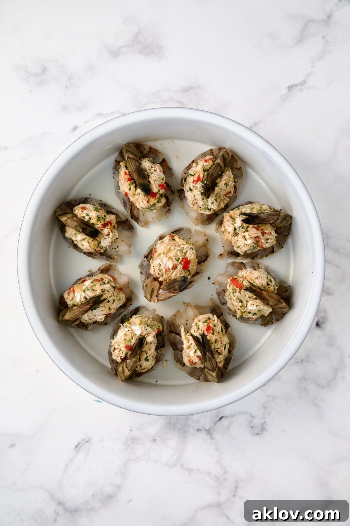 Nine stuffed shrimp arranged in a round white baking dish, ready to be baked.