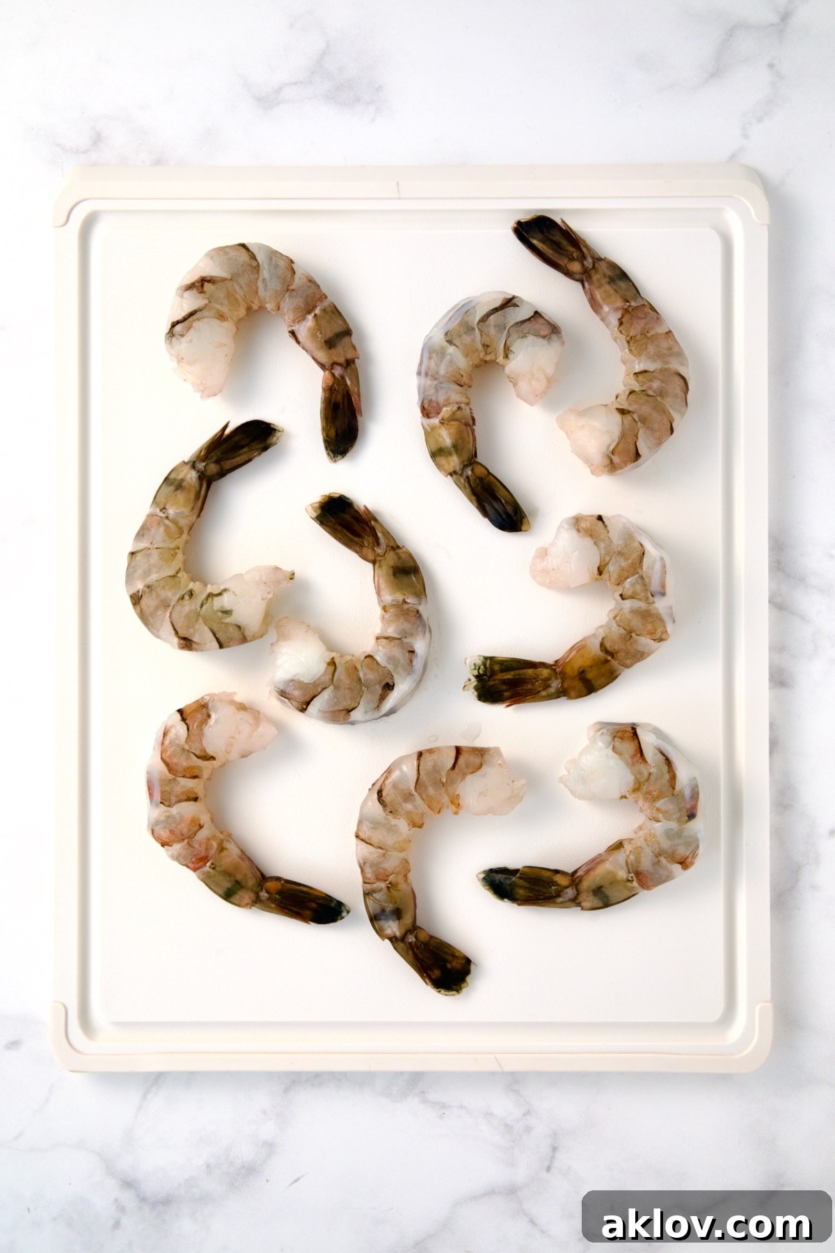 Nine colossal peeled and deveined shrimp on a white plastic cutting board, ready for butterflying.