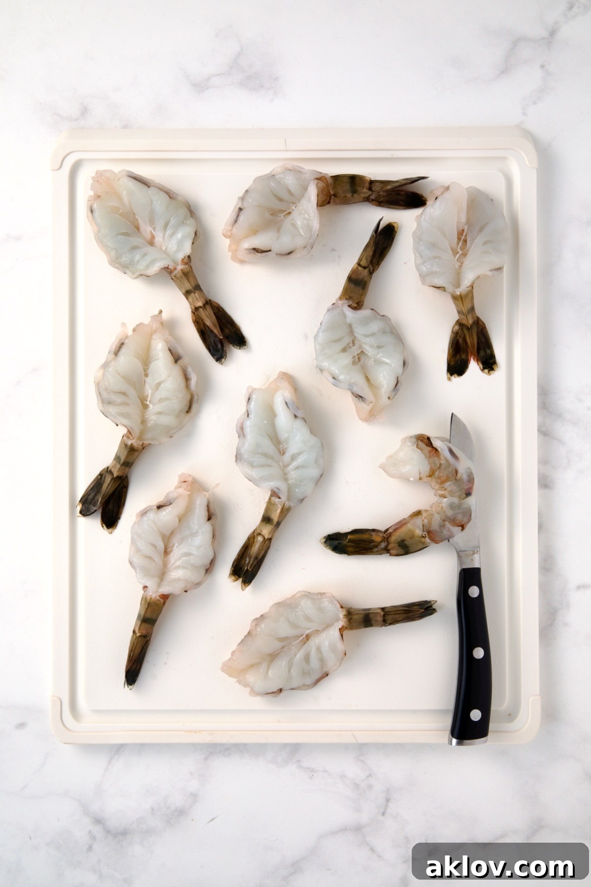 Nine colossal peeled and deveined shrimp on a white plastic cutting board after being butterflied, flattened and prepared for stuffing.