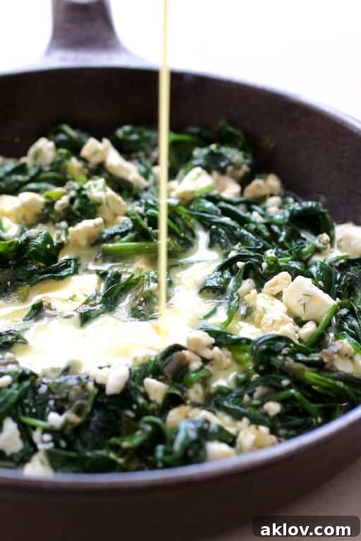 Photo of egg mixture being poured over spinach and leek combination in cast iron skillet, showcasing the cooking process.