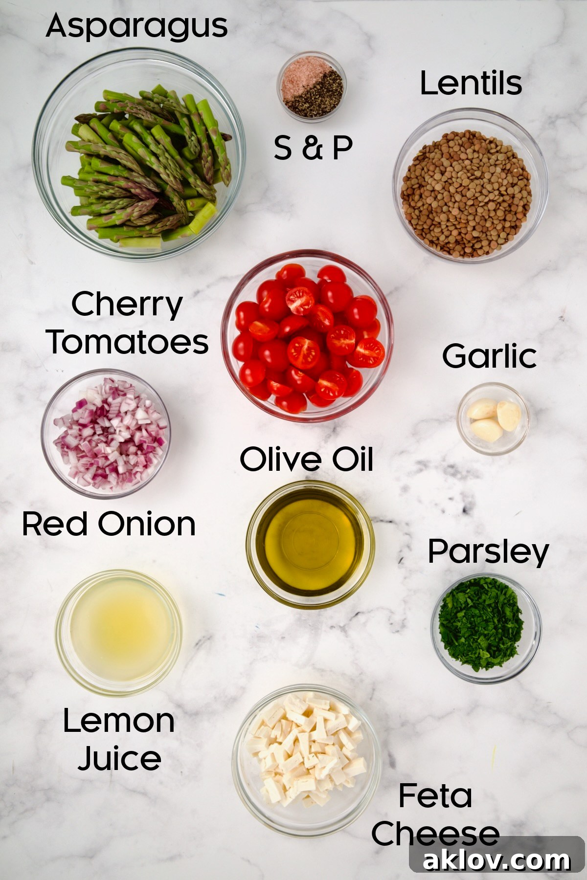 A collection of fresh ingredients for Lemony Lentil Salad, including cooked lentils, blanched asparagus, halved cherry tomatoes, chopped red onion, fresh parsley, lemon, garlic, olive oil, and crumbled feta cheese, arranged in glass bowls.