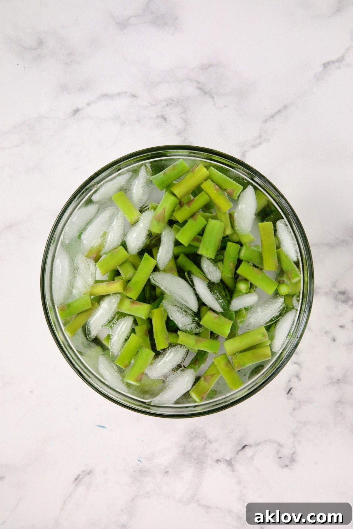 Freshly blanched asparagus cooling in an ice bath within a clear glass bowl, preparing for the Lemony Lentil Salad.