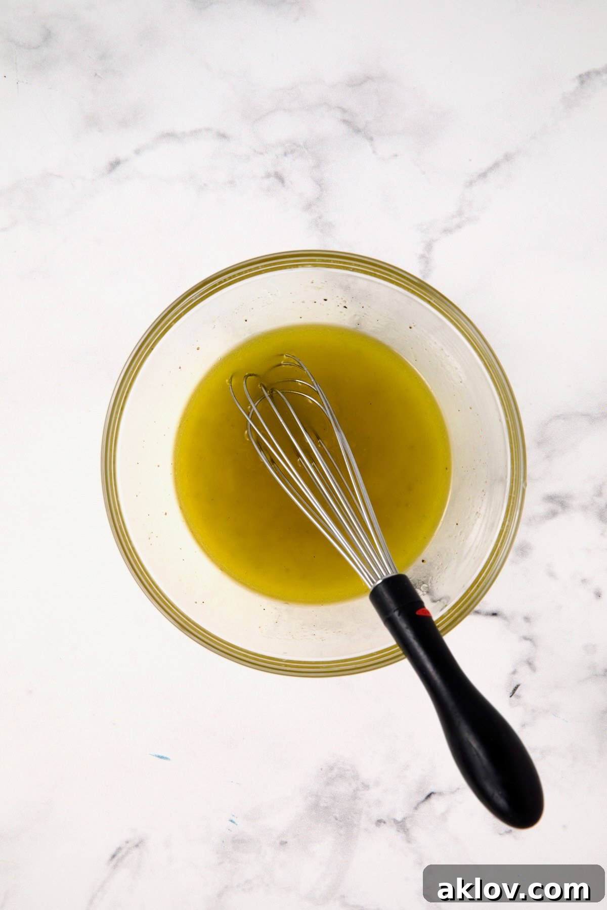 A vibrant lemon vinaigrette, made with fresh lemon juice, extra-virgin olive oil, and minced garlic, being whisked in a clear glass bowl.