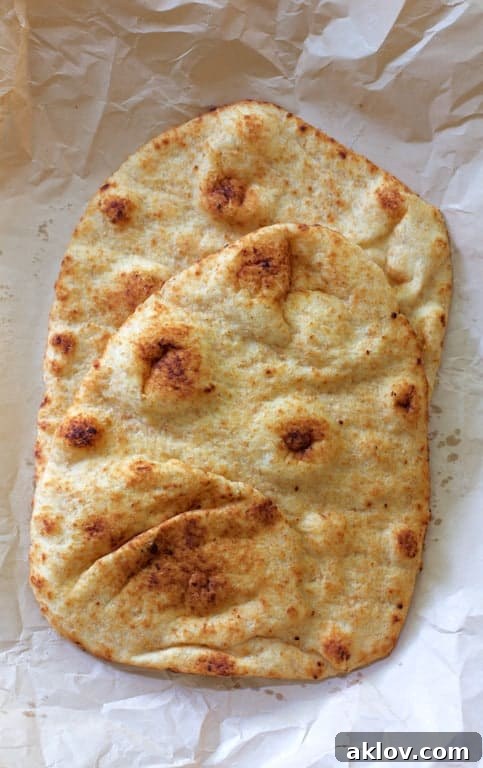 Two pieces of fresh naan bread on parchment paper, ready to be topped for pizza.