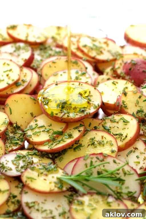 Thinly sliced red potatoes seasoned with fresh rosemary and drizzled with olive oil, ready for roasting.
