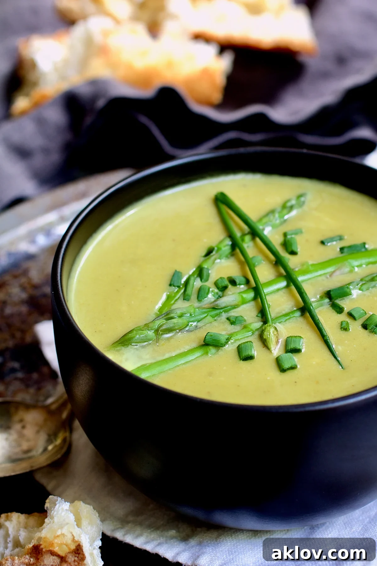 Cream of Asparagus and Leek Soup with Curry in black bowl garnished with chives.