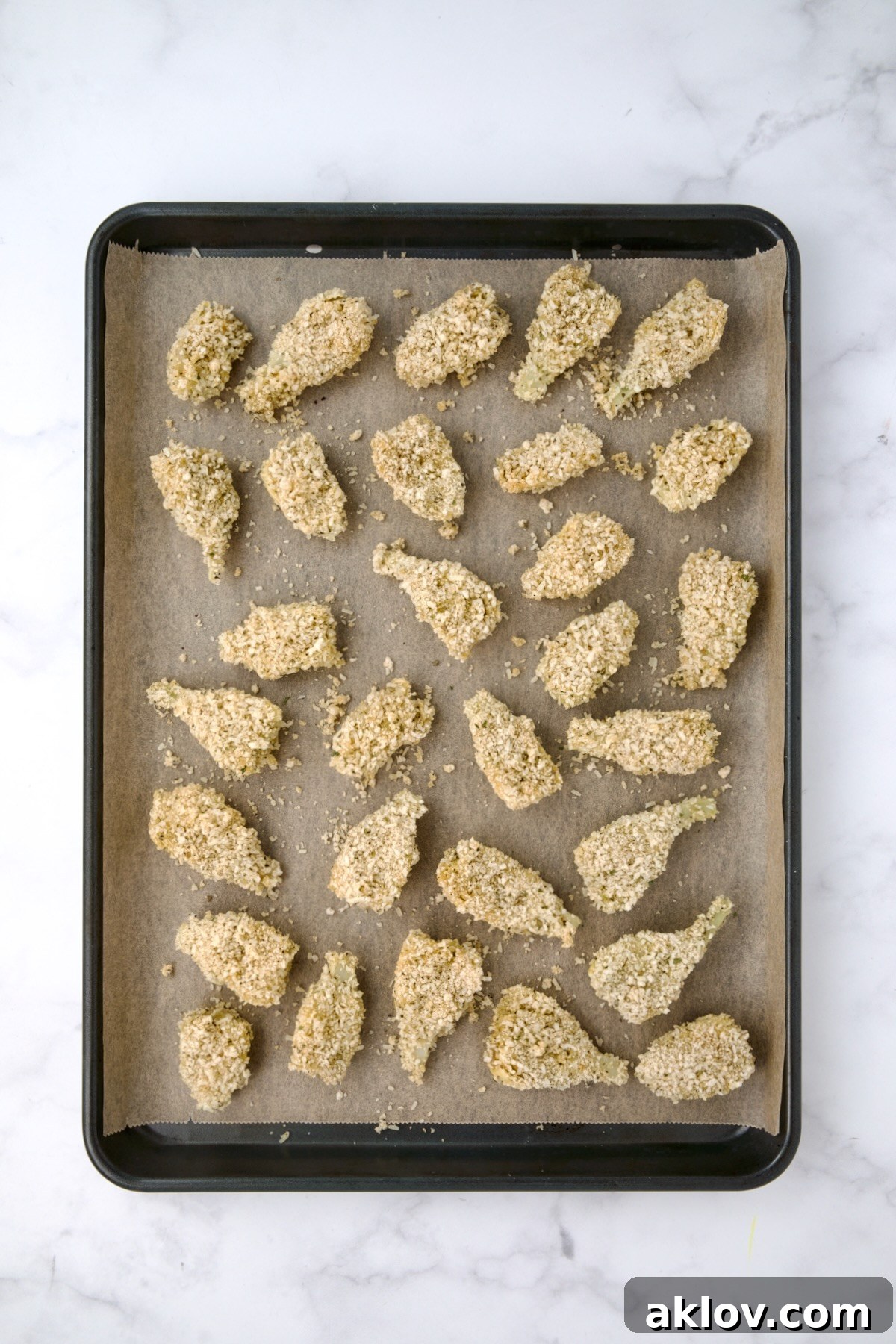 Breaded artichoke hearts on parchment paper-lined baking sheet before being baked.