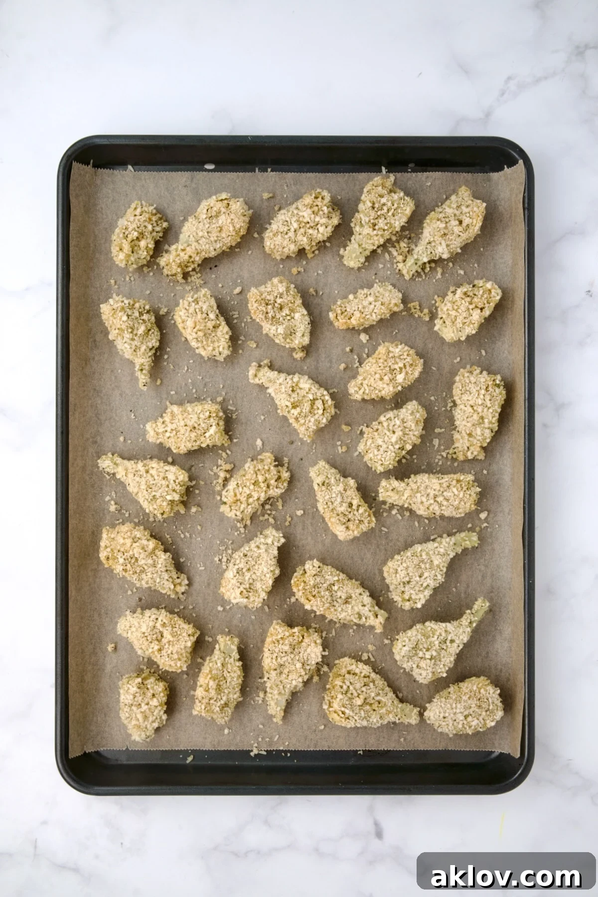 Breaded artichoke hearts on parchment paper-lined baking sheet before being baked.