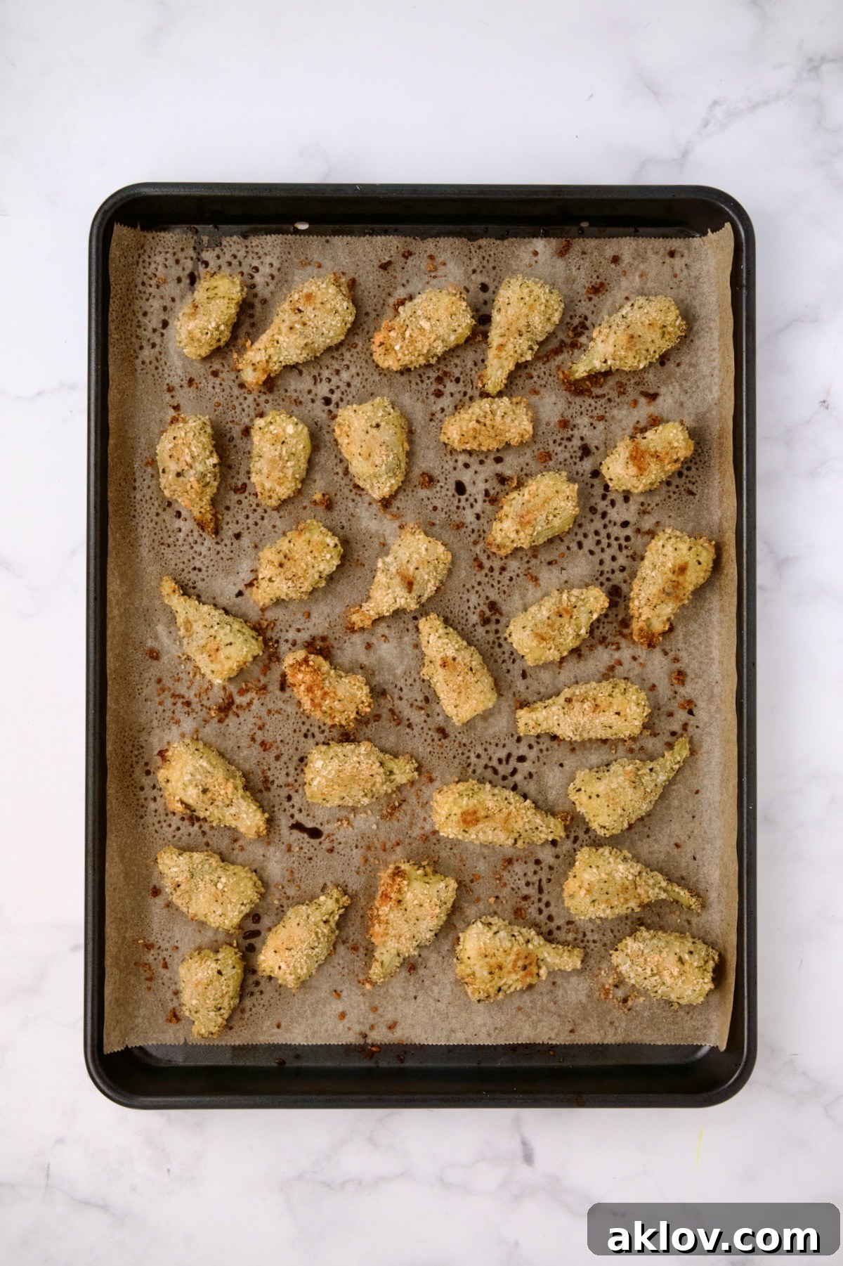 Breaded artichoke hearts on parchment paper-lined baking sheet after being baked.