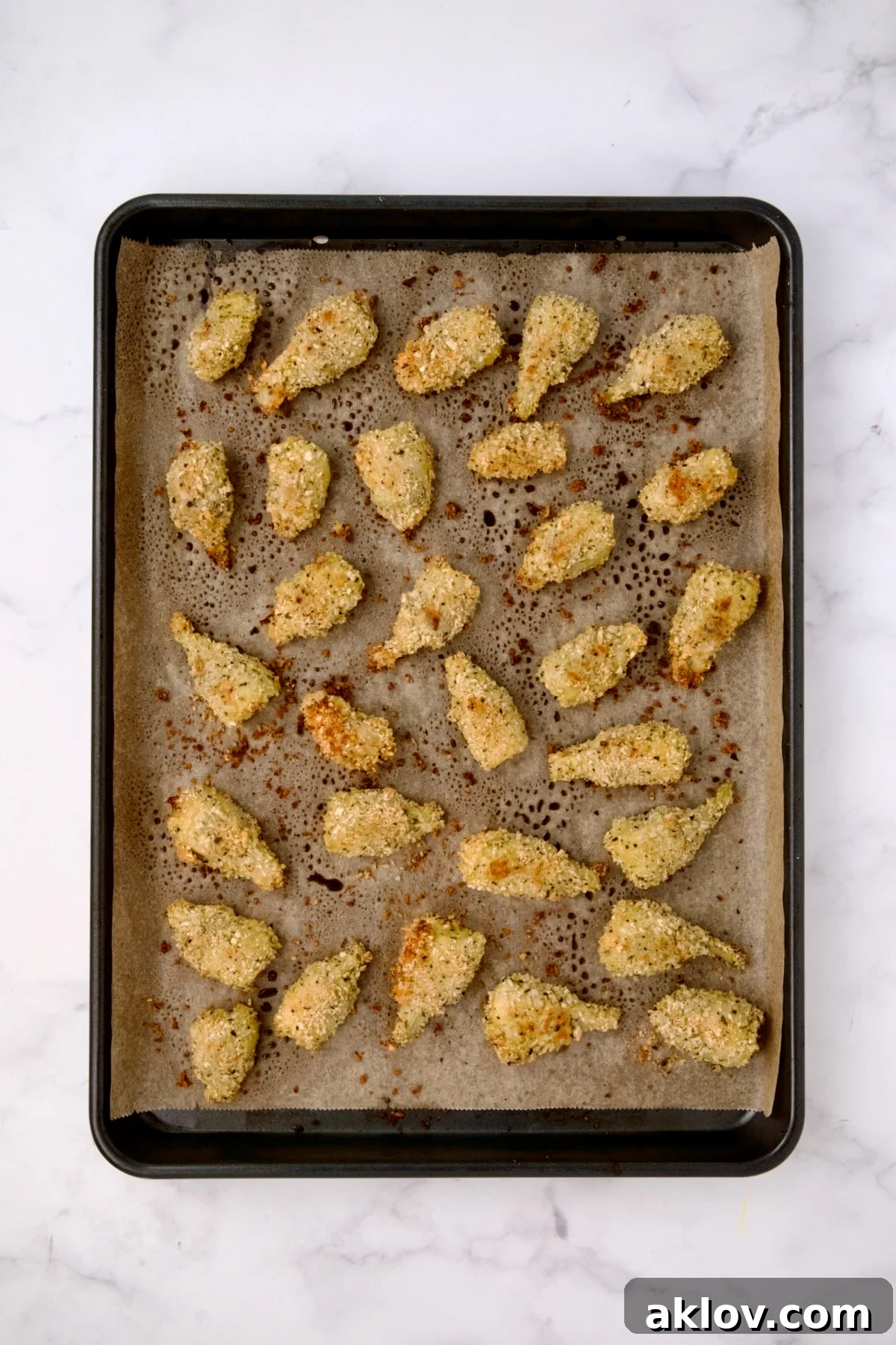 Breaded artichoke hearts on parchment paper-lined baking sheet after being baked.
