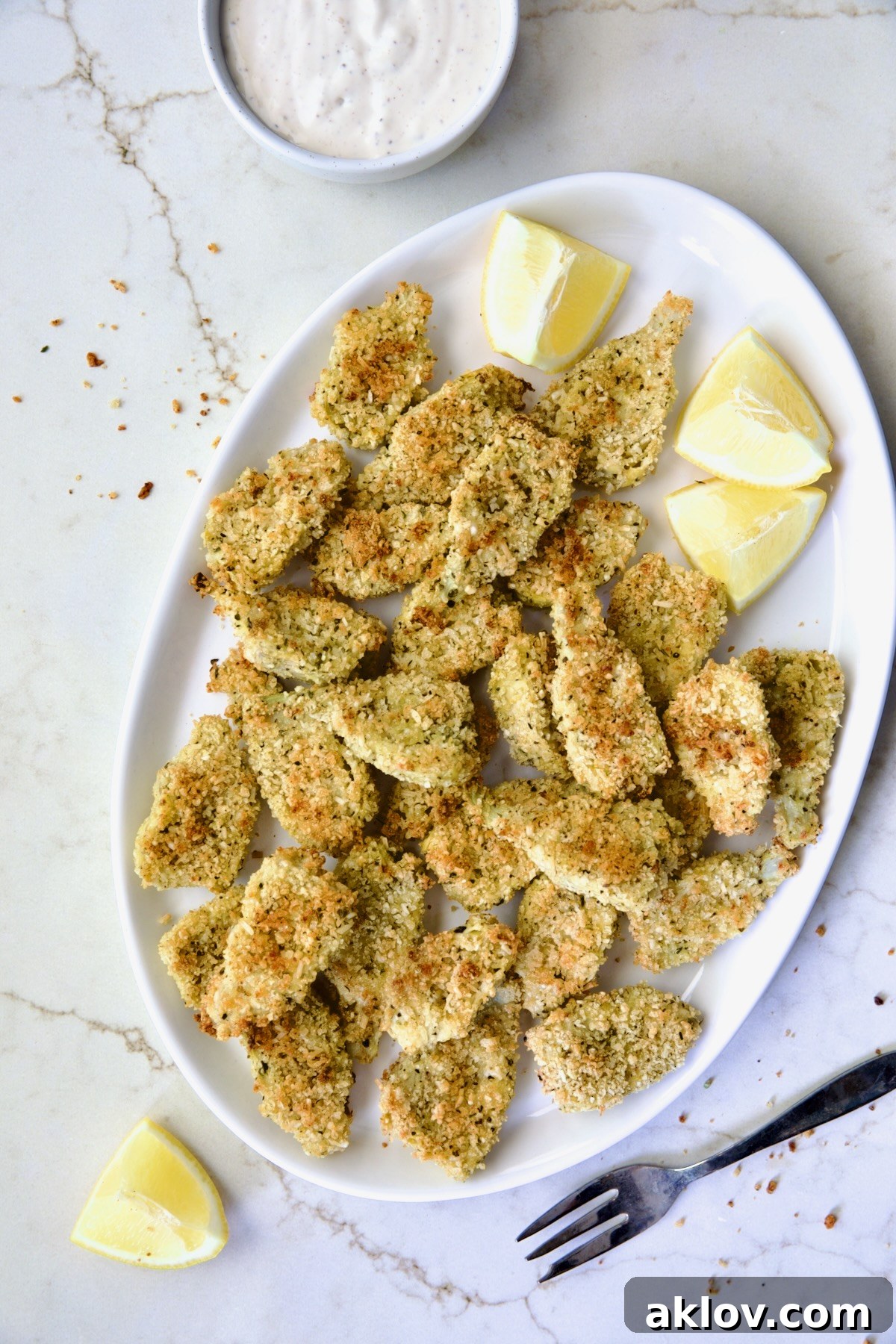 Crispy Parmesan Artichoke Hearts on oval white platter with lemon wedges.
