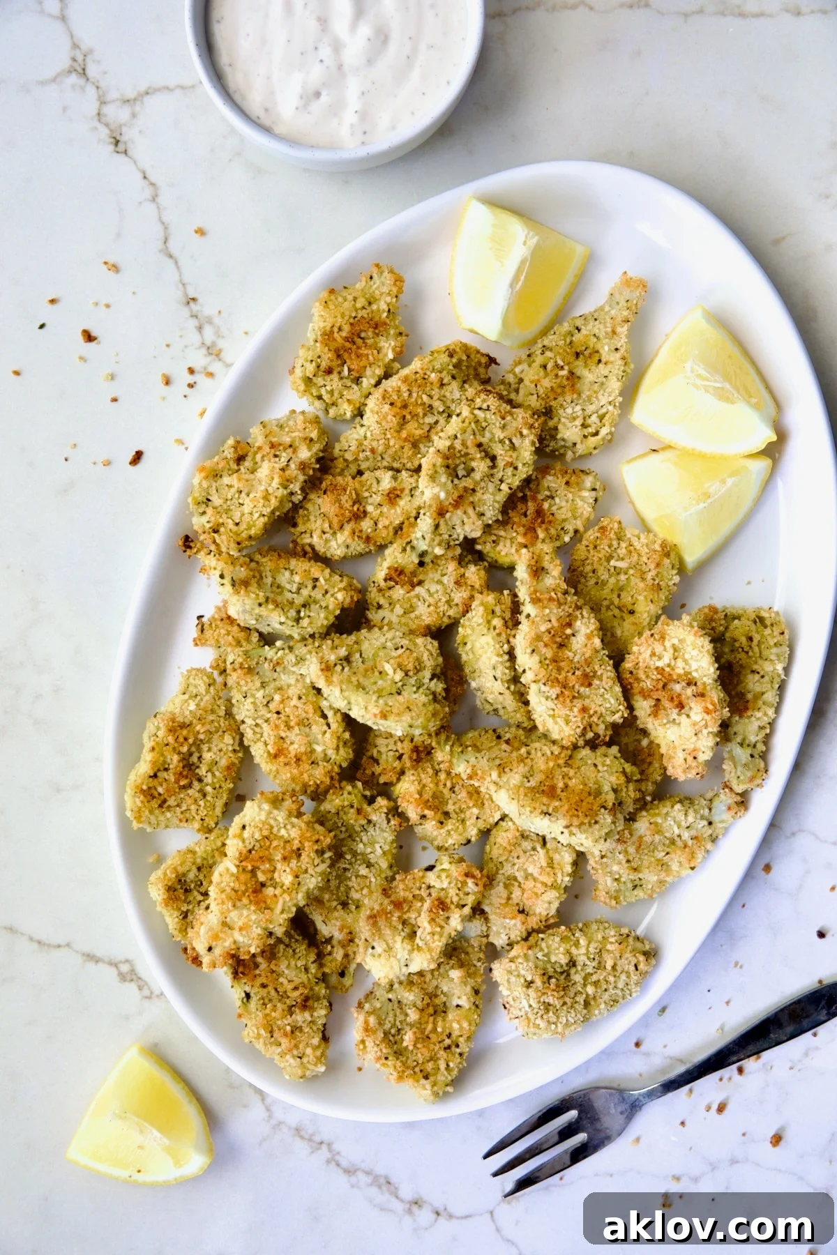 Crispy Parmesan Artichoke Hearts on oval white platter with lemon wedges.