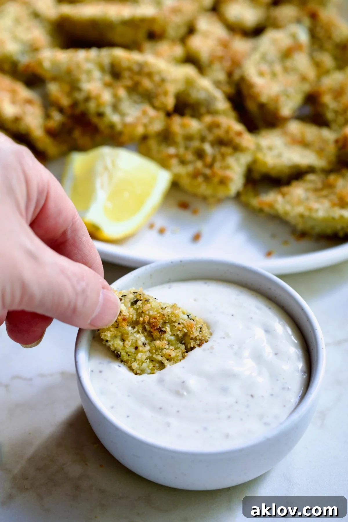 Hand dipping an artichoke heart into the Caesar dip in a white bowl.