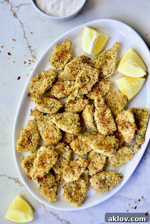 Crispy Parmesan Artichoke Hearts on oval white platter with lemon wedges.
