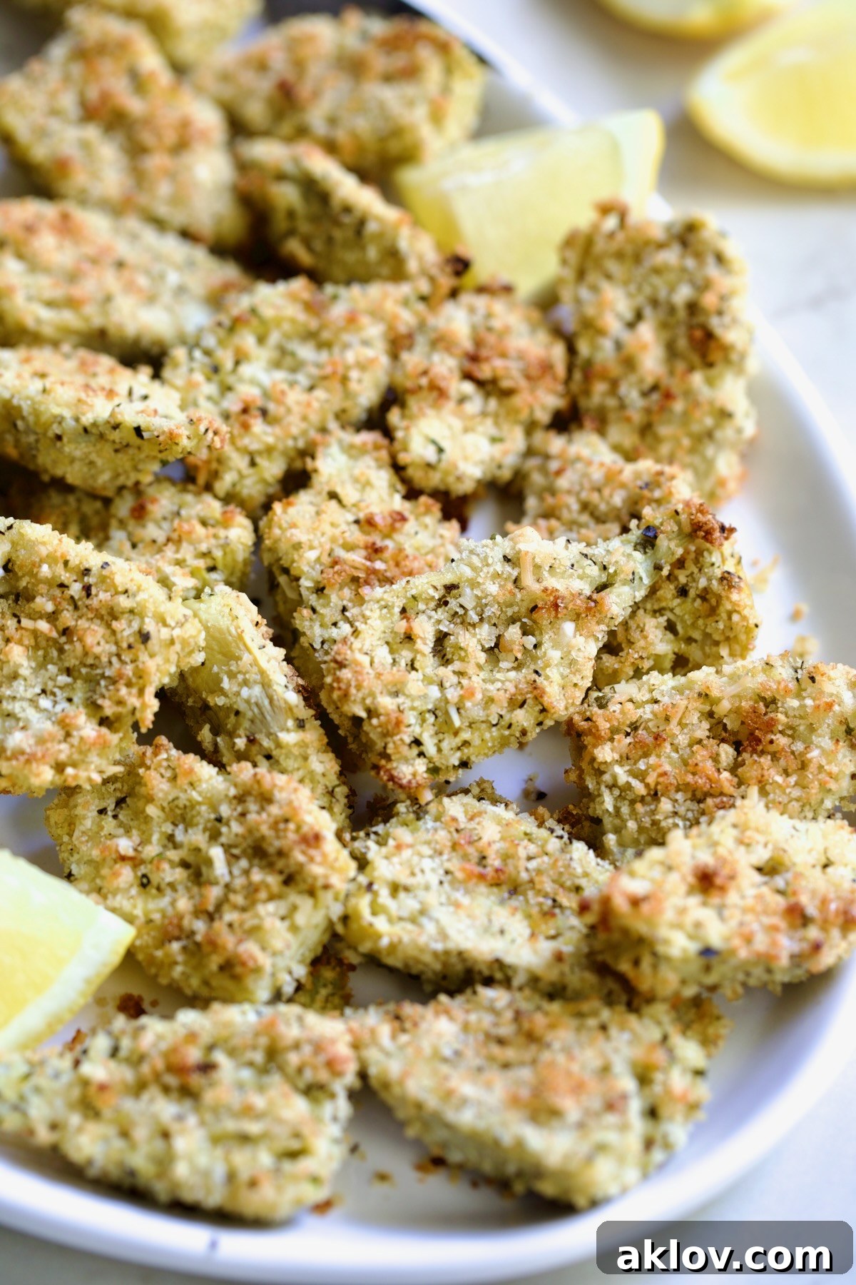 Crispy Parmesan Artichoke Hearts on oval white platter with lemon wedges.