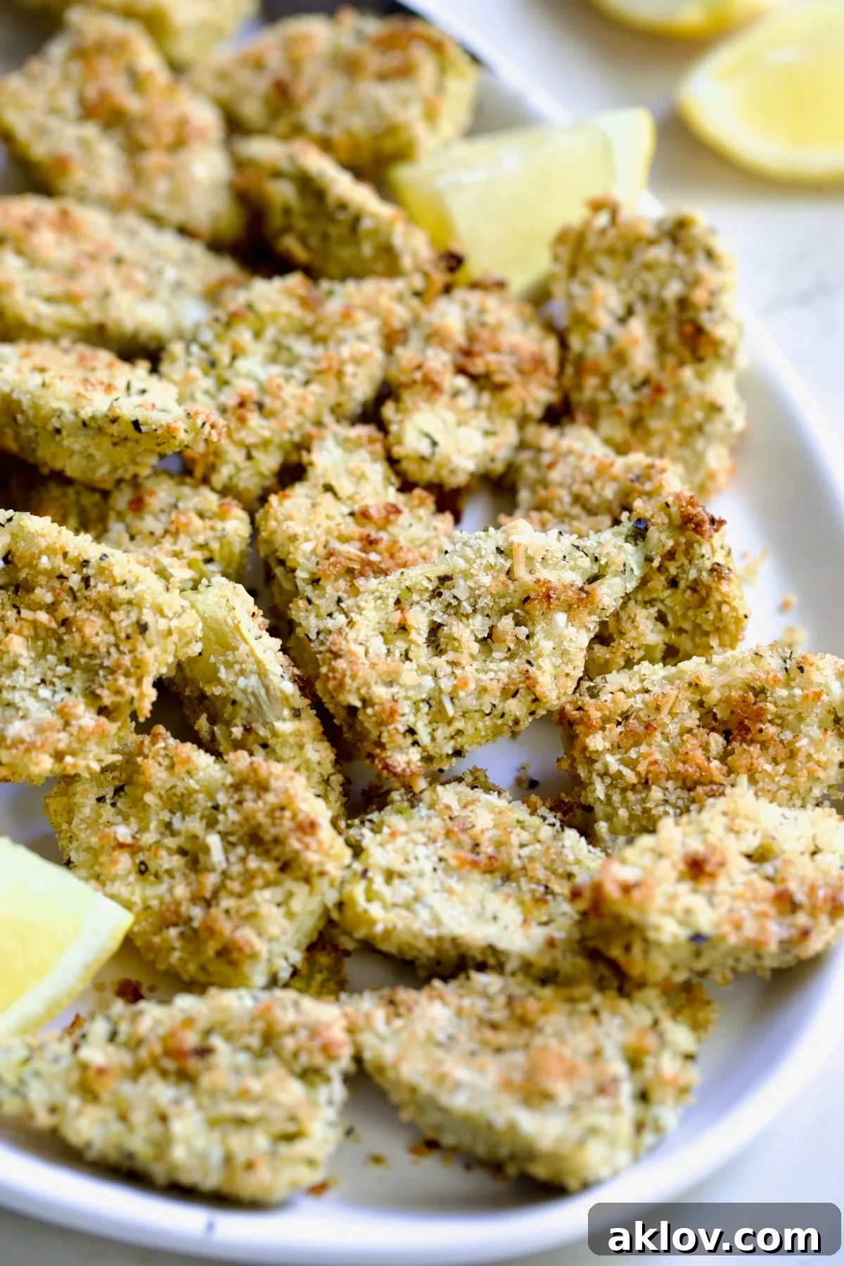 Crispy Parmesan Artichoke Hearts on oval white platter with lemon wedges.