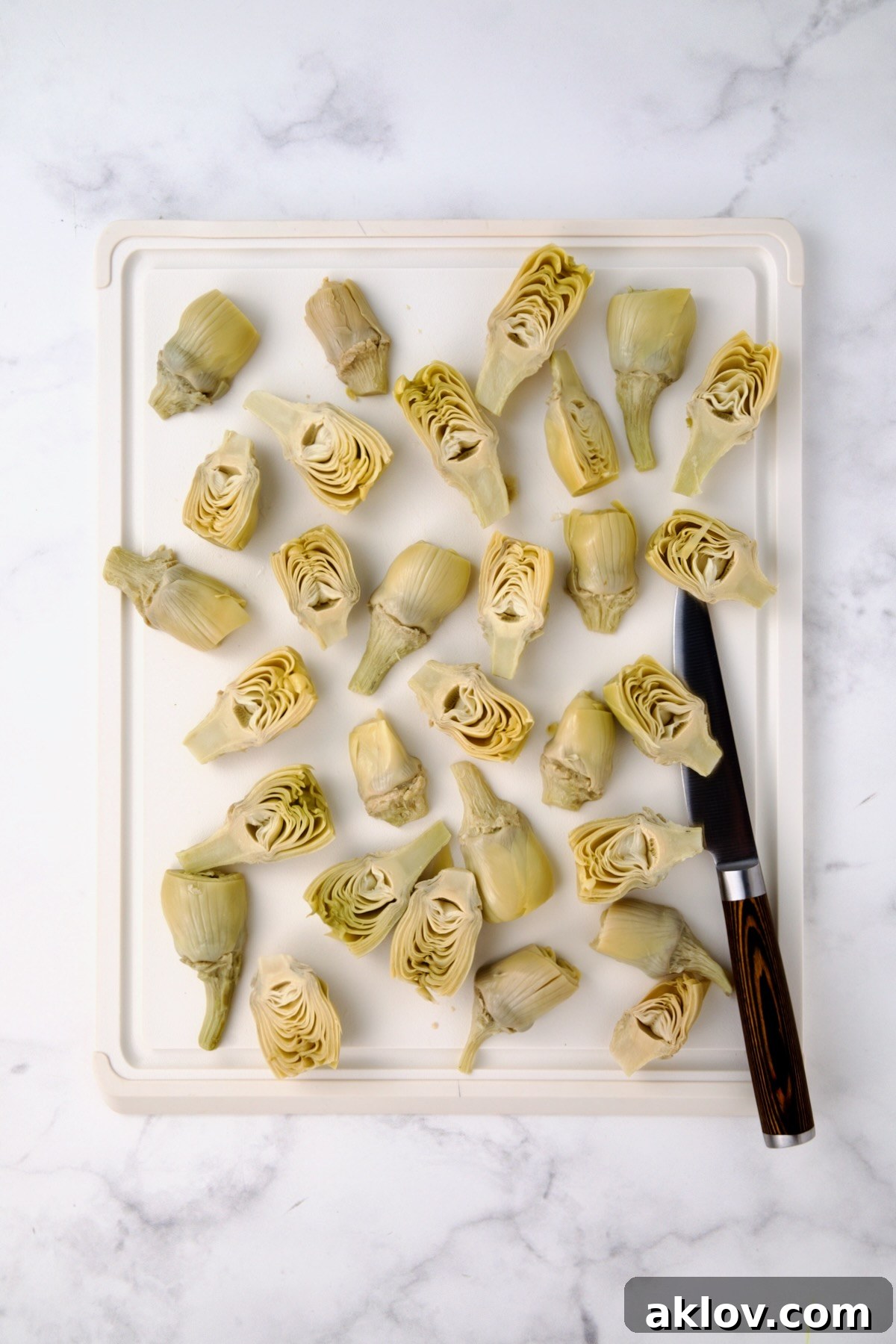 Halved artichoke hearts on white plastic cutting board.