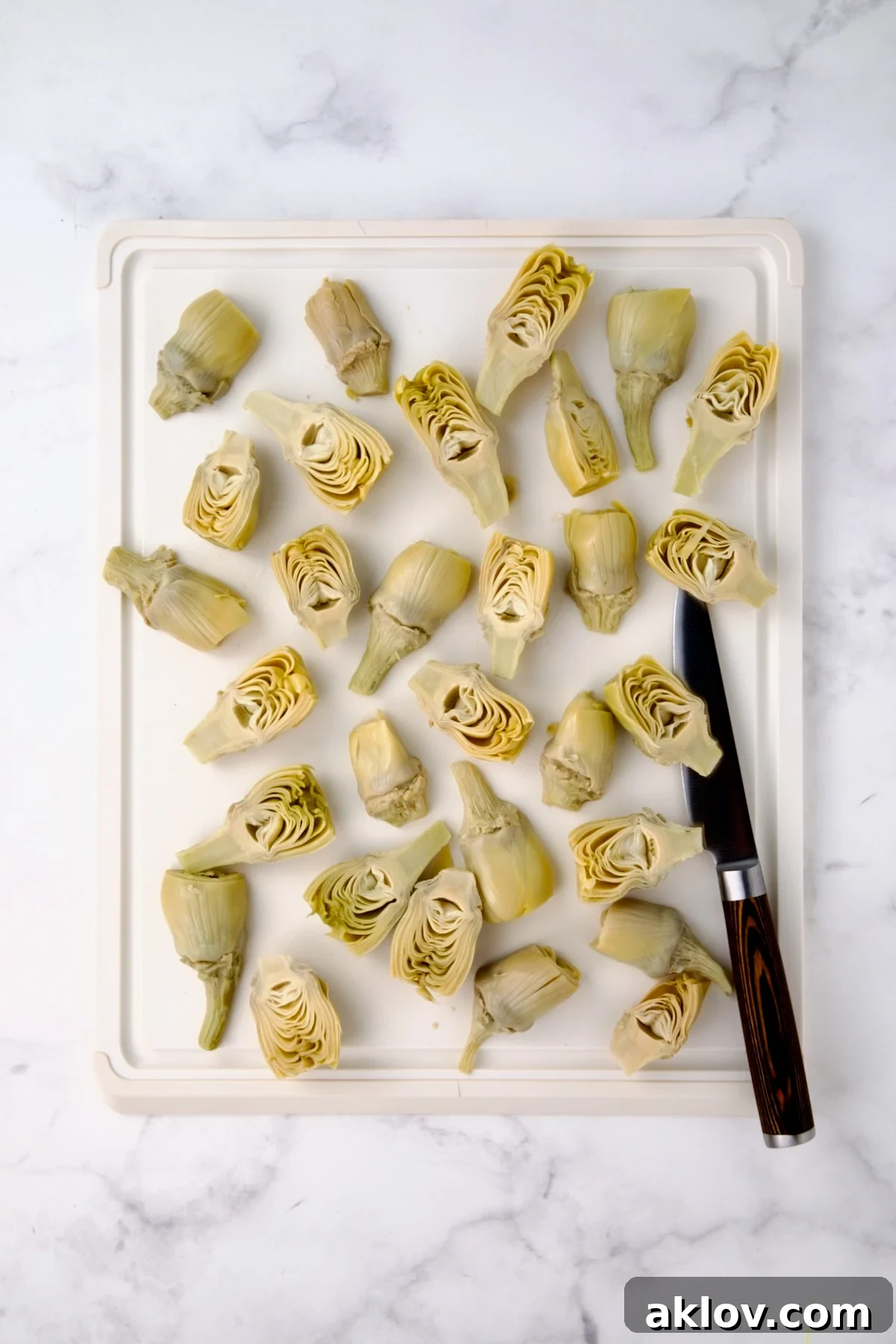 Halved artichoke hearts on white plastic cutting board.