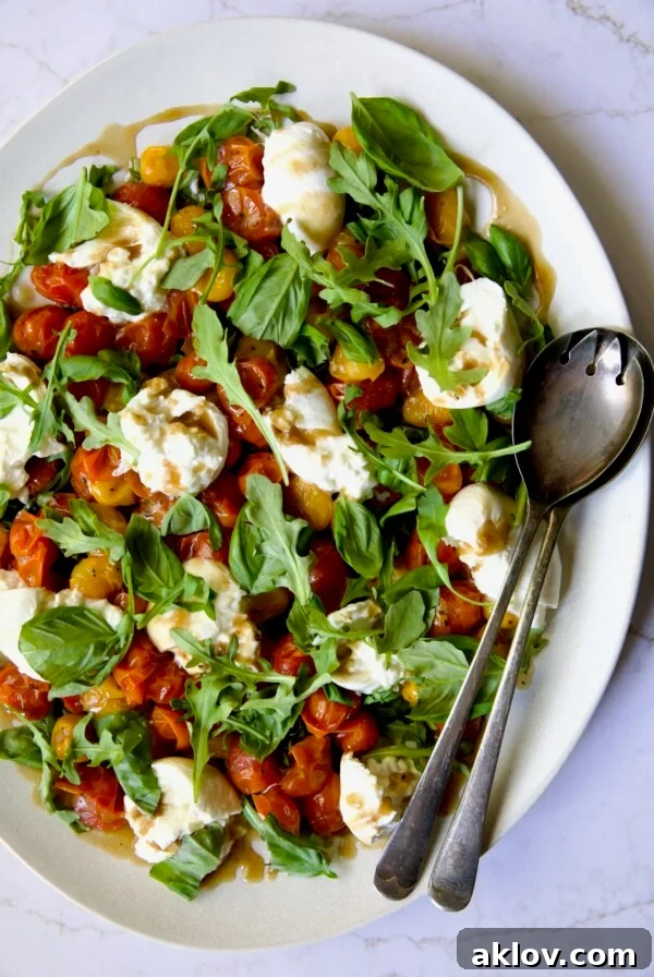 Roasted Cherry Tomato Burrata Caprese Salad on white oval platter with serving utensils.