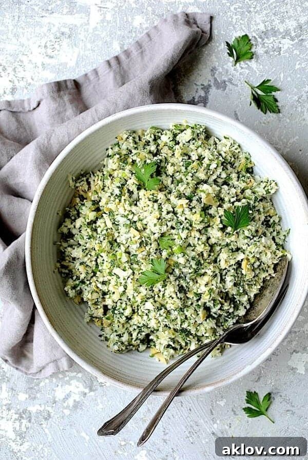 Cauliflower Artichoke Tabbouleh in white serving bowl with serving utensils garnished with fresh parsley.
