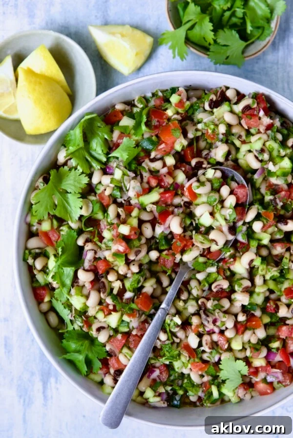 Black-Eyed Pea Salad in white bowl with lemon wedges and cilantro in bowls.