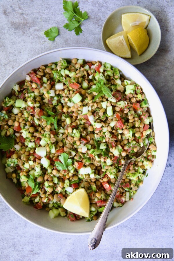 Lentil Tabbouleh in white bowl garnished with fresh mint sprigs and lemon wedges.