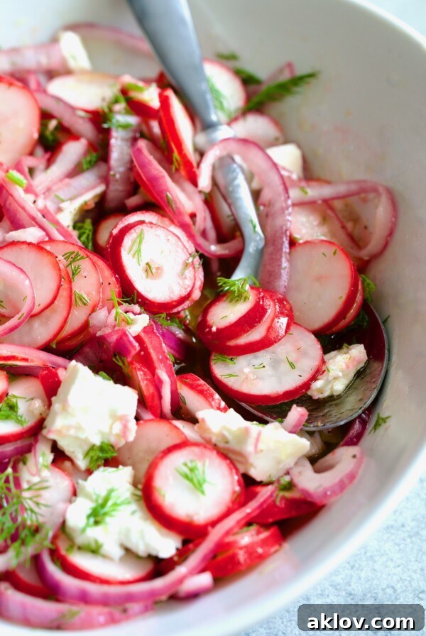 Radish Red Onion Salad in white oval serving bowl with serving spoon garnished with fresh dill.